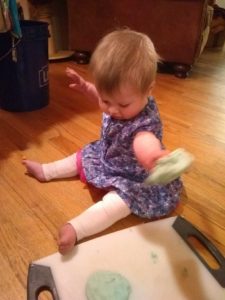 Child in blue dress and white pants throws their edible play dough.