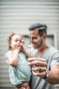 a male prsenting adult holds up a sparkler for a child to see