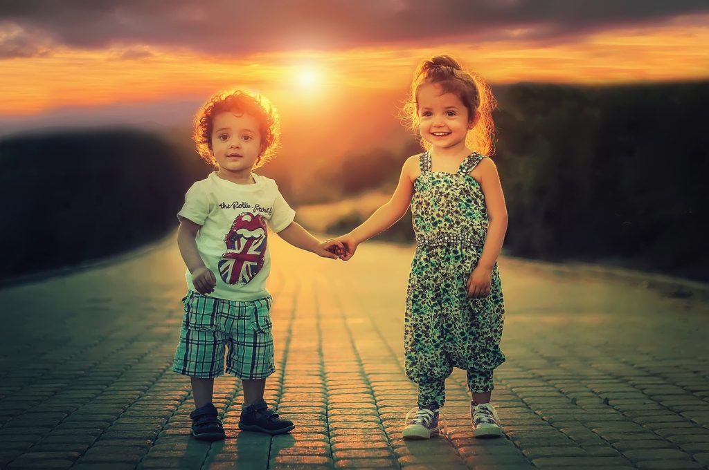 2 young children hold hands with a sunset in the background