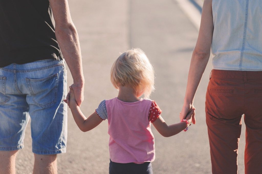 a child walk with 2 adults while holding hands