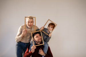An older male, midle aged man, and male child each hold a hallow picture frame around their face