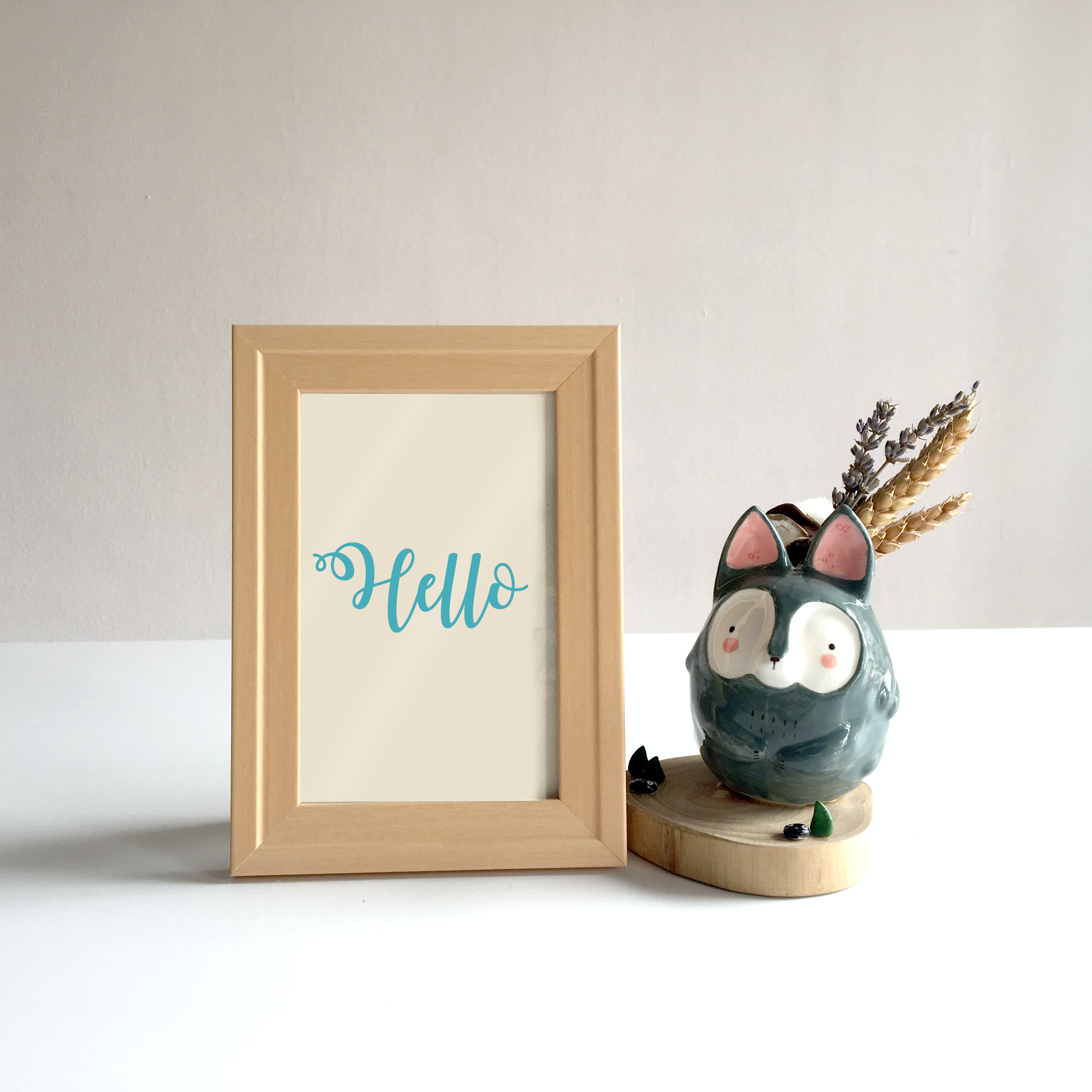 The word "hello" written is swirly writing sits in a beige picture frame with a small wooden animal sitting beside it.