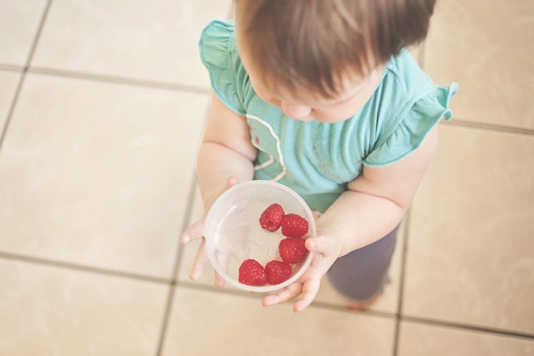 a young child holds a bowl of raspberries
