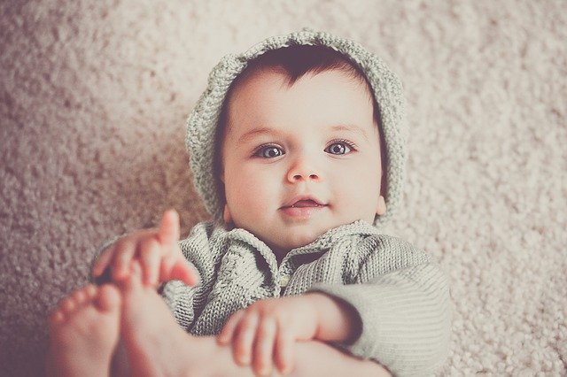 a blue eyed baby looks up at the camera while grabbing their toes