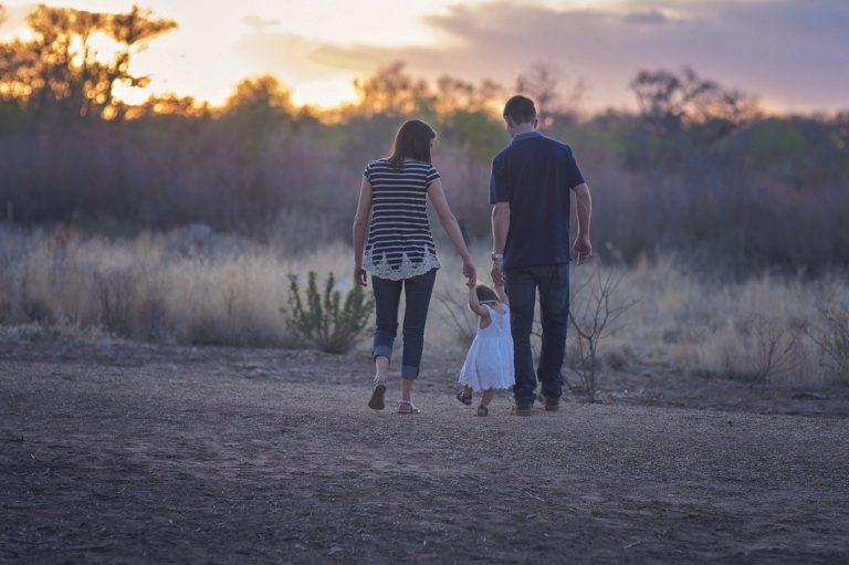 2 adults and a child walk towards a sunset