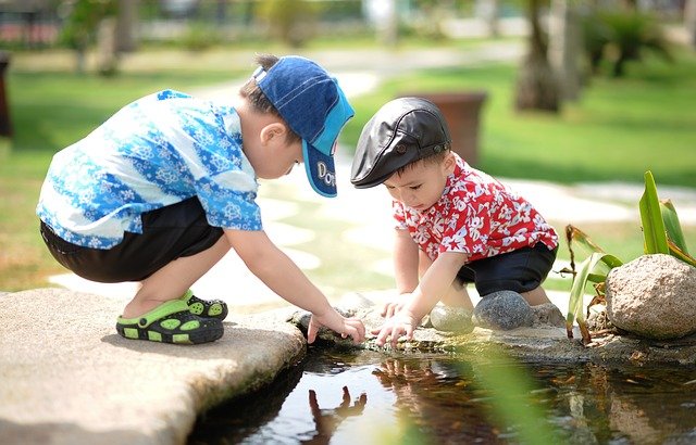 Two children crouch by water, playing and exploring