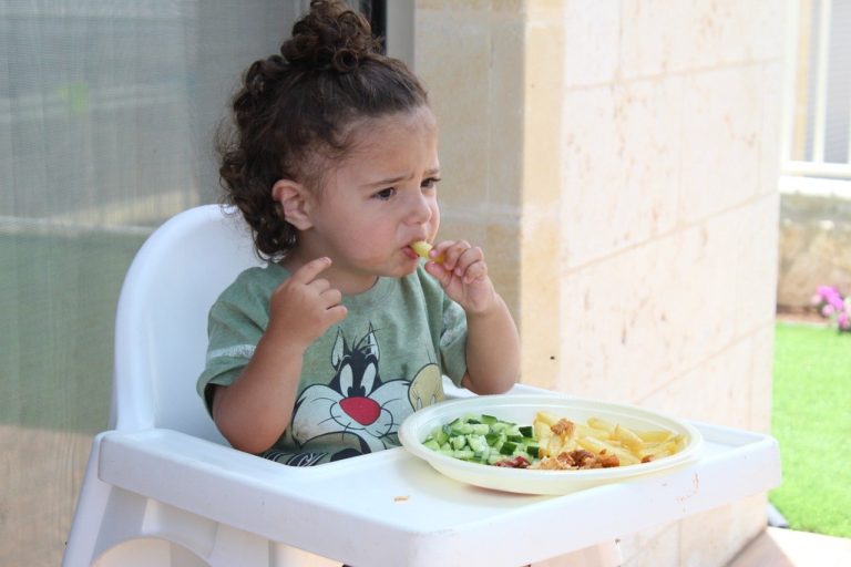 Child sits in high chair with plate of food in front of them