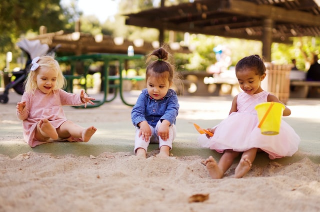 Three children sit and play in a sandbox