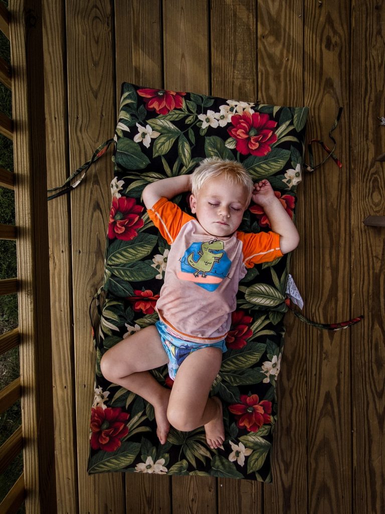 A toddler sleeps on a mat on the floor instead of in a toddler bed