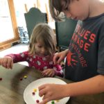 Two children work together to put skittles on a plate