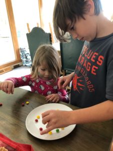 Two children work together to put skittles on a plate
